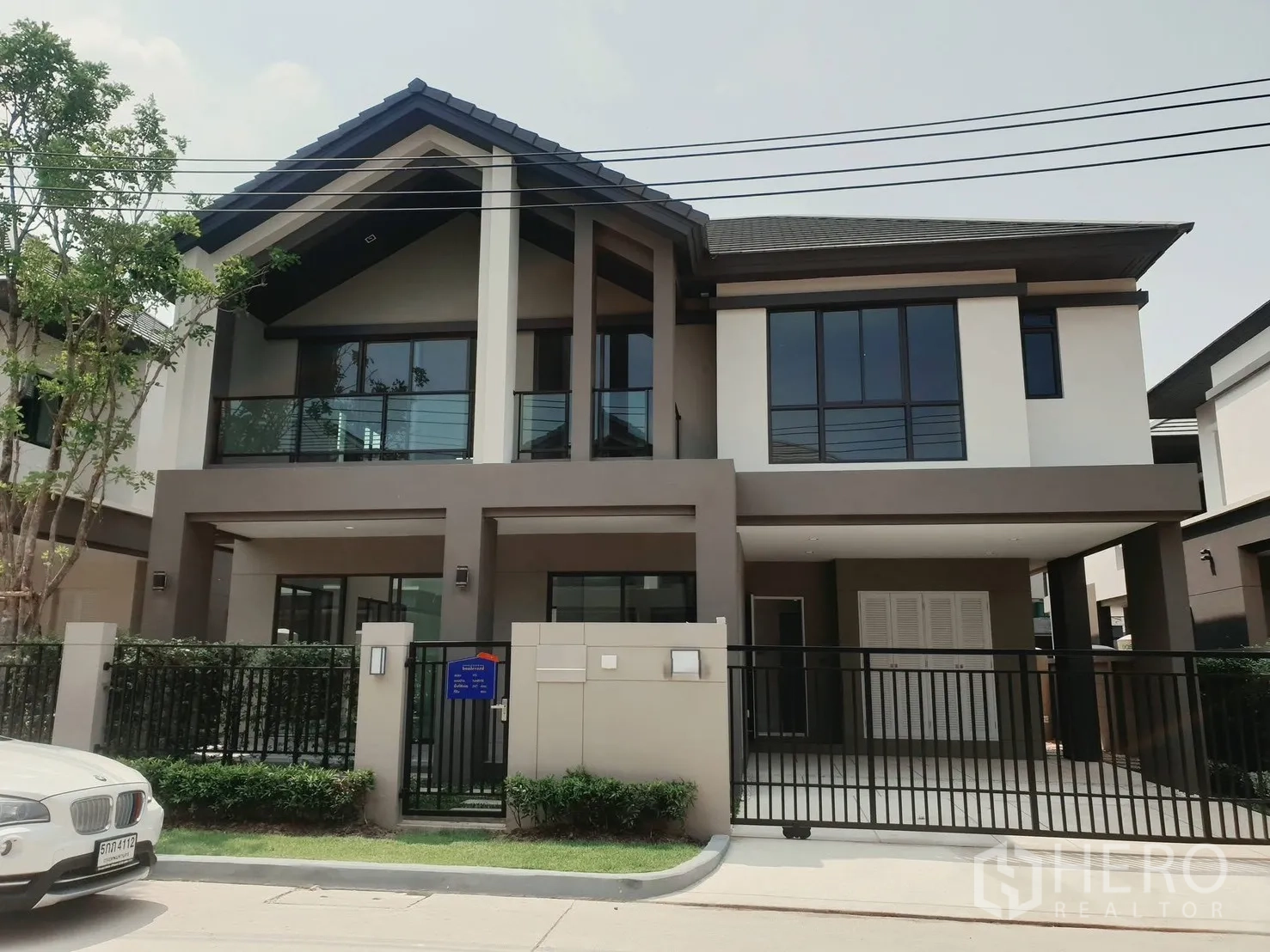 Detached House for rent in Saphan Sung, Bangkok - Front view of modern detached house with glass balcony and wide driveway behind black gate.