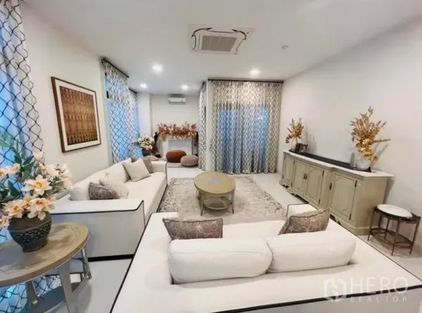 Detached House for rent or sale in Saphan Sung, Bangkok - Bright living room with white sofas, patterned curtains, recessed lights and a sideboard.