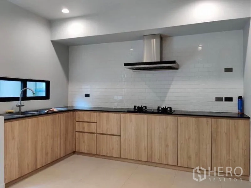 Townhouse for rent in Suan Luang, Bangkok - L-shaped modern kitchen with wood cabinets, gas hob and stainless range hood