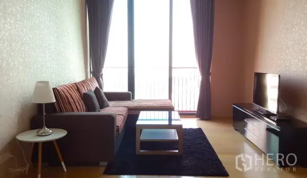 Condominium for rent in Phaya Thai, Bangkok - Living room with L-shaped sofa, glass coffee table, TV console and floor-to-ceiling windows.