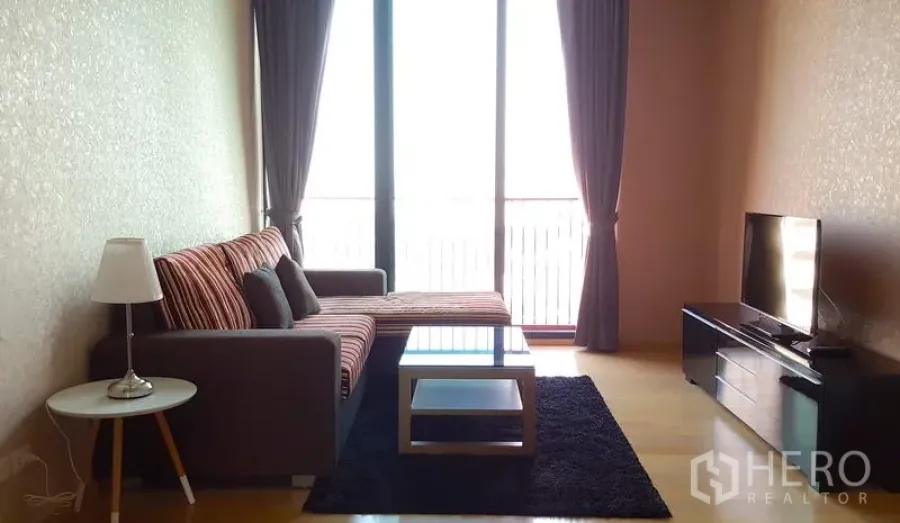Condominium for rent in Phaya Thai, Bangkok - Living room with L-shaped sofa, glass coffee table, TV console and floor-to-ceiling windows.