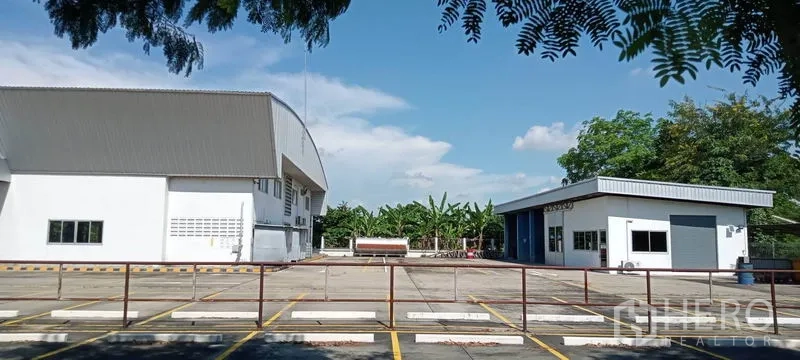 Warehouse for rent or sale in Lam Luk Ka, Pathum Thani - Expansive loading yard between the main warehouse and a separate office or workshop building.