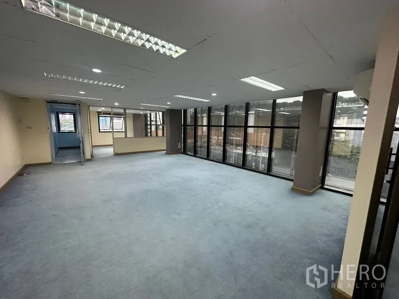 Office Space for rent in Bang Rak, Bangkok - Spacious open-plan office with carpet flooring, recessed fluorescent lighting and a wall of windows.