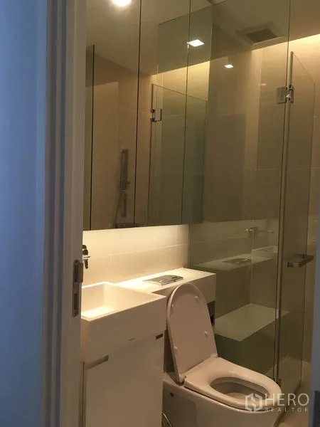 Condominium for rent or sale in Chatuchak, Bangkok - Modern bathroom with a glass-enclosed shower, wall-mounted vanity and toilet.
