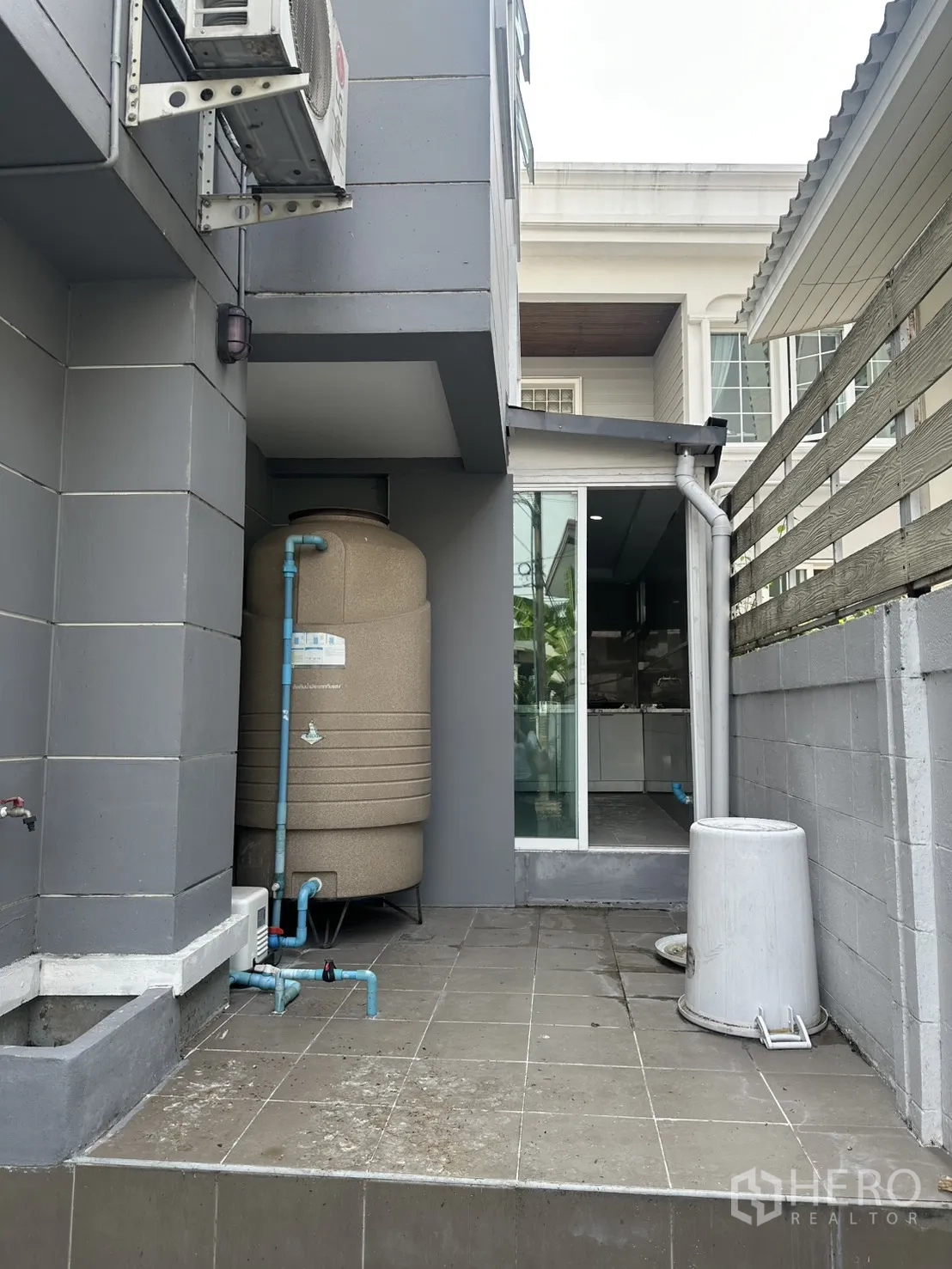 โฮมออฟฟิศ for rent in Watthana, Bangkok - มุมซักล้างนอกบ้านพร้อมถังเก็บน้ำ ท่อประปาสีฟ้า พื้นกระเบื้อง และประตูกระจกบานเลื่อน