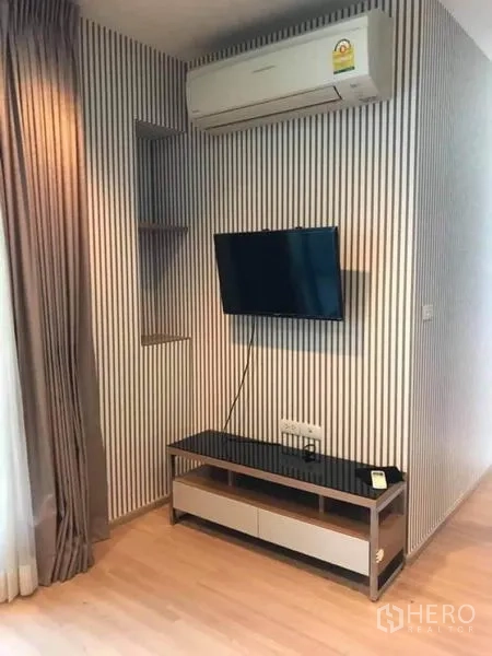 Condominium for rent or sale in Phaya Thai, Bangkok - TV corner with wall-mounted screen, striped feature wall, air conditioner and console.
