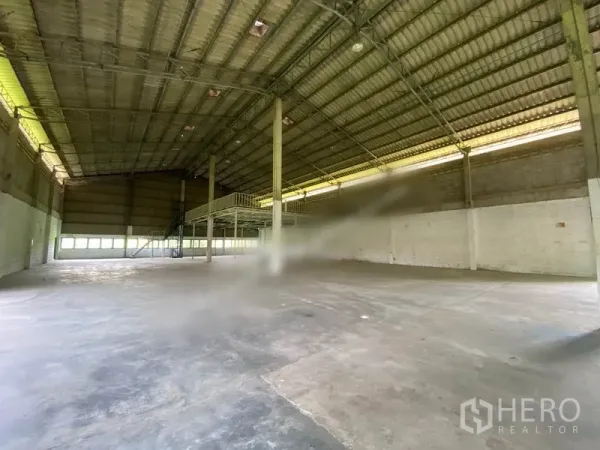 Warehouse for rent in Khlong Sam Wa, Bangkok - Spacious warehouse interior with high steel truss roof, polished concrete floor, and a mezzanine platform with staircase.
