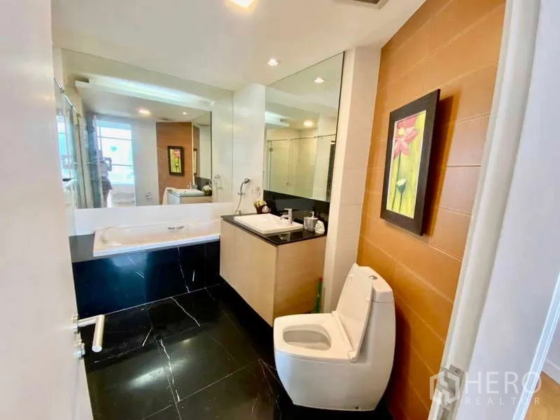 Condominium for rent or sale in Sathon, Bangkok - Bathroom with bathtub, vanity, and toilet, warm accent wall and large mirror.