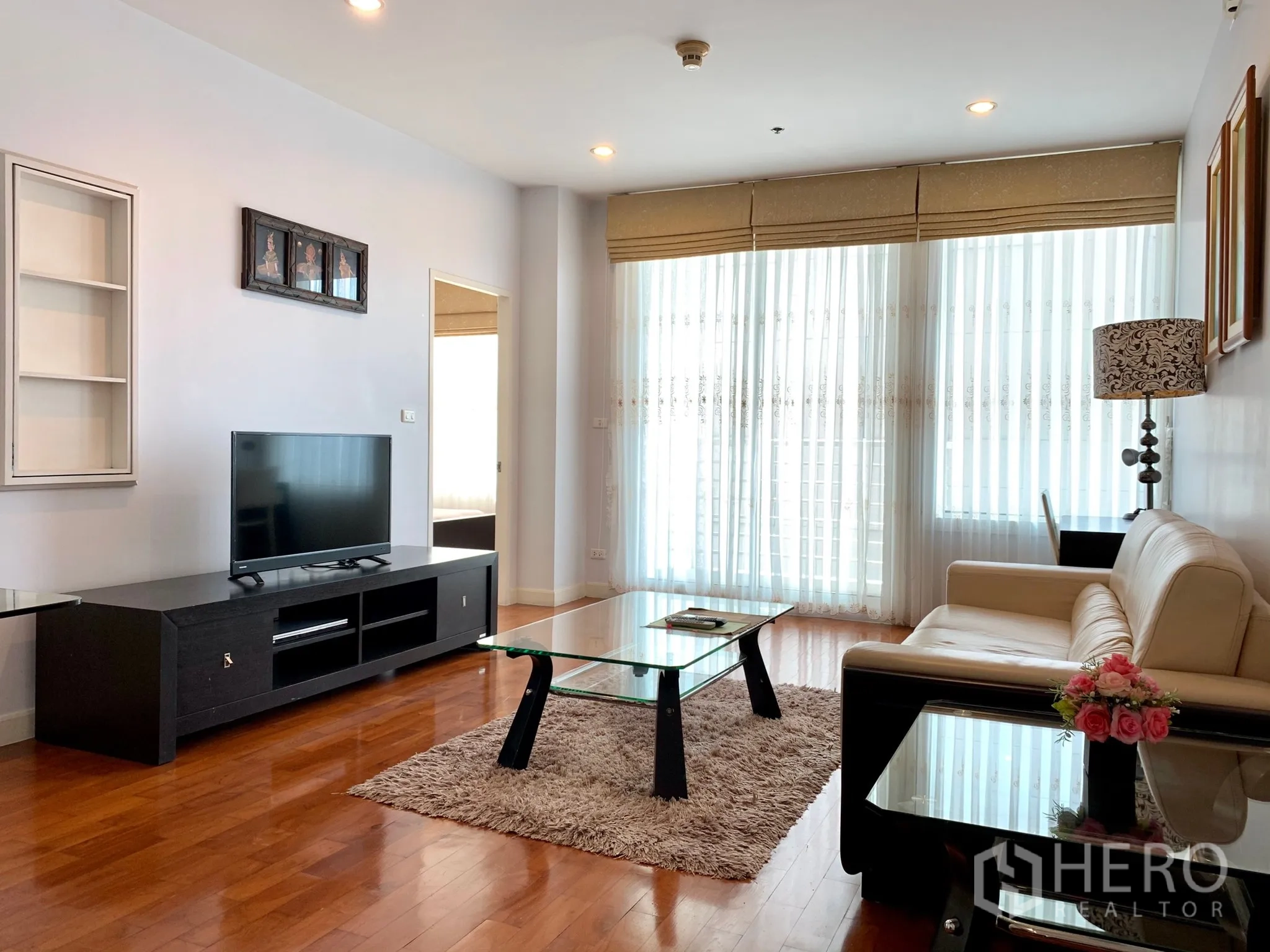 Condominium for rent in Khlong Toei, Bangkok - Bright living room with floor-to-ceiling windows, beige sofa, TV console, glass coffee table and wood flooring in a Bangkok condo.