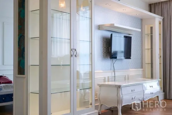 Condominium for rent in Khlong Toei, Bangkok - Living room feature wall with white built-in display cabinets, mounted TV, and classic console.