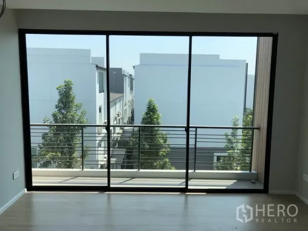 联排别墅 出售在Saphan Sung, Bangkok - 室内大玻璃门连通阳台，俯瞰绿树与成排联排屋景观。