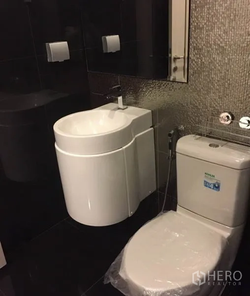 Condominium for rent in Khlong Toei, Bangkok - Modern bathroom with dark tiles, vanity sink and toilet.