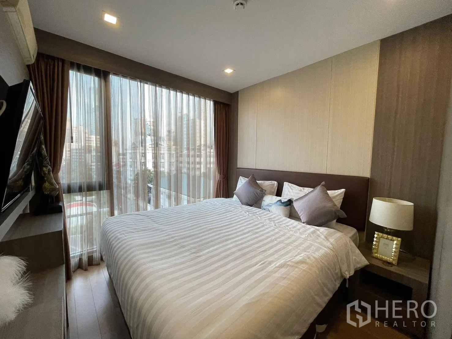 คอนโด for rent in Watthana, Bangkok - ห้องนอนเตียงขนาดใหญ่ มีโต๊ะข้างเตียงและโคมไฟ มองเห็นวิวเมืองผ่านผ้าม่านโปร่ง