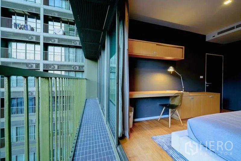 Condominium for rent in Watthana, Bangkok - Bedroom balcony with green railings and sliding glass doors beside a long work desk.