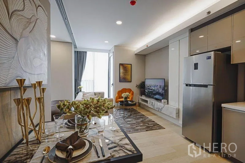 Condominium for sale in Khlong Toei, Bangkok - Dining table beside the kitchen looking toward the living room with TV console and balcony light.