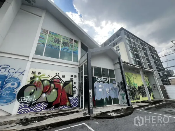 Retail Space for rent in Watthana, Bangkok - Angled view of the glass-fronted façade with graffiti and a neighboring condominium.