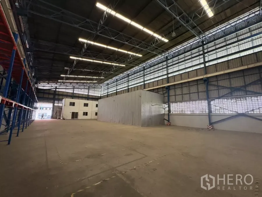 Warehouse for rent in Mueang Samut Prakan, Samut Prakan - High-ceiling warehouse interior with skylights, pallet racks and an attached office block.