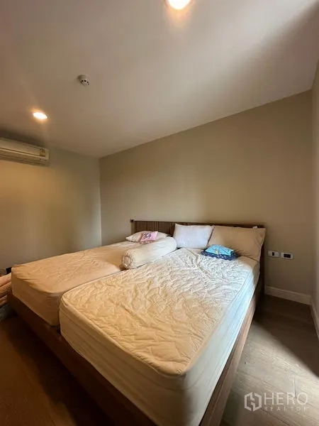 Condominium for rent in Khlong Toei, Bangkok - Second bedroom with twin mattresses, warm lighting and wall-mounted air-conditioner.