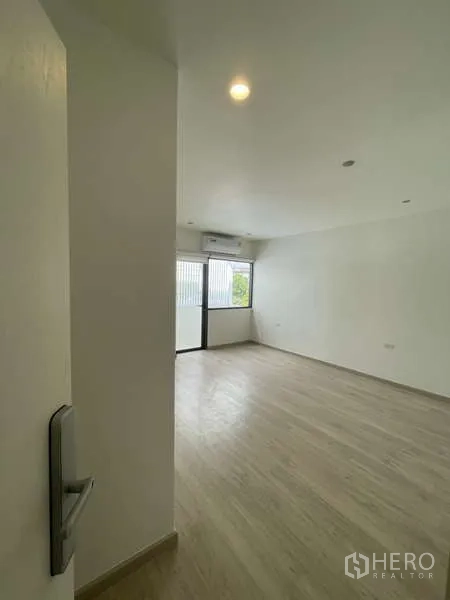 Home Office for rent in Don Mueang, Bangkok - Spacious bedroom with wood floors, balcony door and wall-mounted air conditioner.