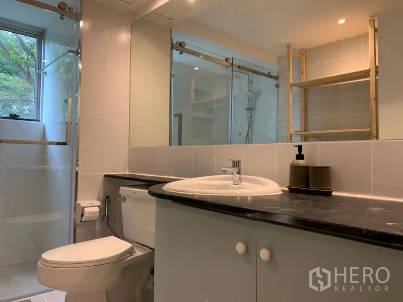 Condominium for sale in Watthana, Bangkok - Bathroom with black countertop vanity, toilet and glass shower enclosure.