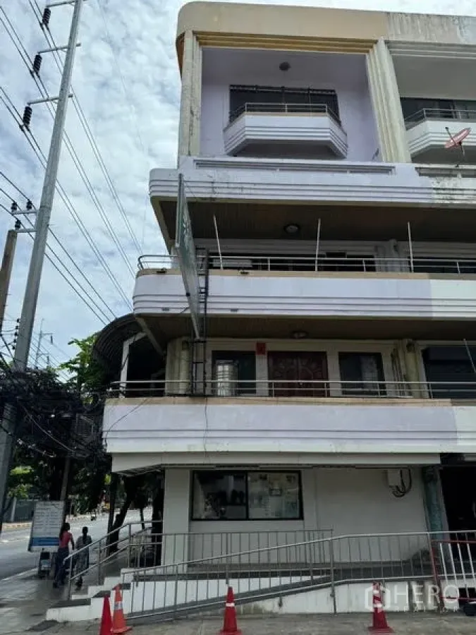 Shophouse for rent in Watthana, Bangkok - Side view of a multi-level building with balconies and a front ramp.