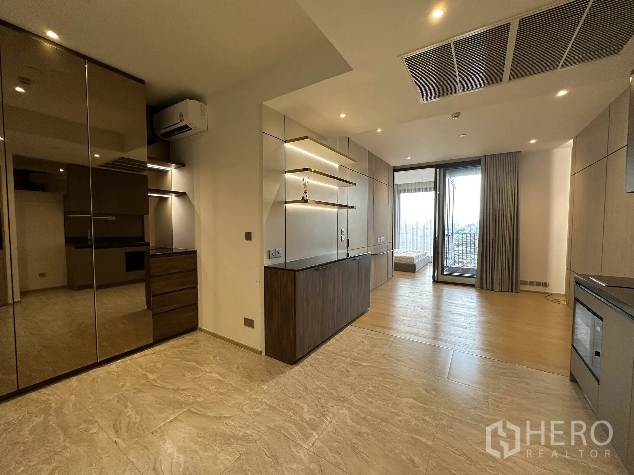 Condominium for sale in Din Daeng, Bangkok - Wide view of living space with built-in shelving, glossy wardrobes, and sliding door to a balcony with city outlook.