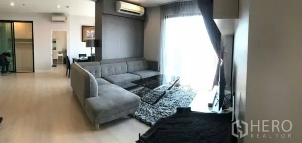 公寓 出租或出售在Huai Khwang, Bangkok - 明亮客厅，L形沙发、长绒地毯与落地阳台窗。