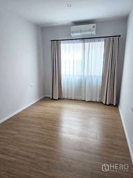 Townhouse for rent in Suan Luang, Bangkok - Bright empty room with wood floors, curtained window and wall-mounted air conditioner.