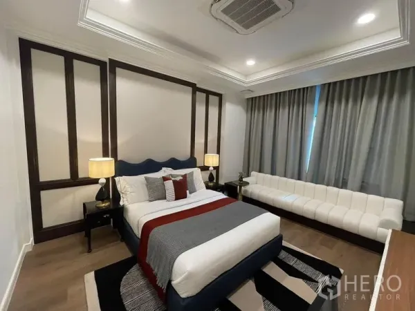 Detached House for rent or sale in Saphan Sung, Bangkok - Cozy bedroom with tray ceiling, upholstered bed and a long white sofa beside full-length curtains.