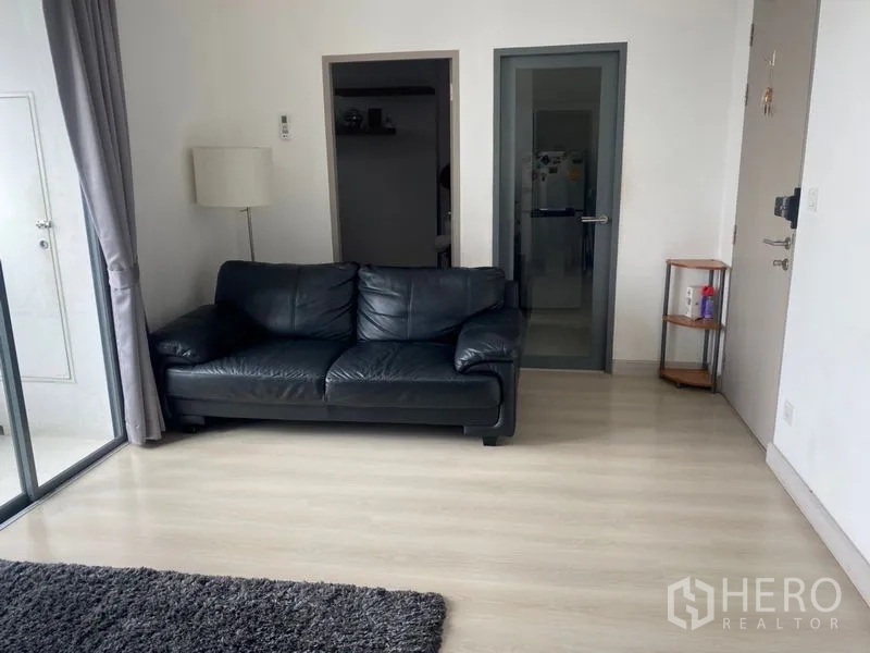 Condominium for sale in Phra Khanong, Bangkok - Cozy living room with black leather sofa beside sliding glass doors