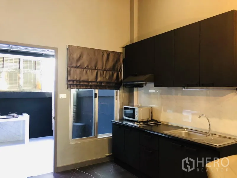 Townhouse for rent in Bang Kapi, Bangkok - Indoor kitchen with black cabinetry, sink, range hood and window to terrace.