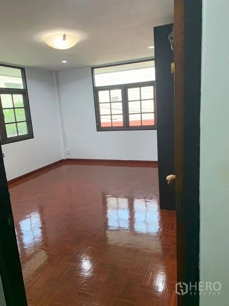 Detached House for rent in Khlong Toei, Bangkok - Sunlit bedroom with glossy parquet floor and two windows.