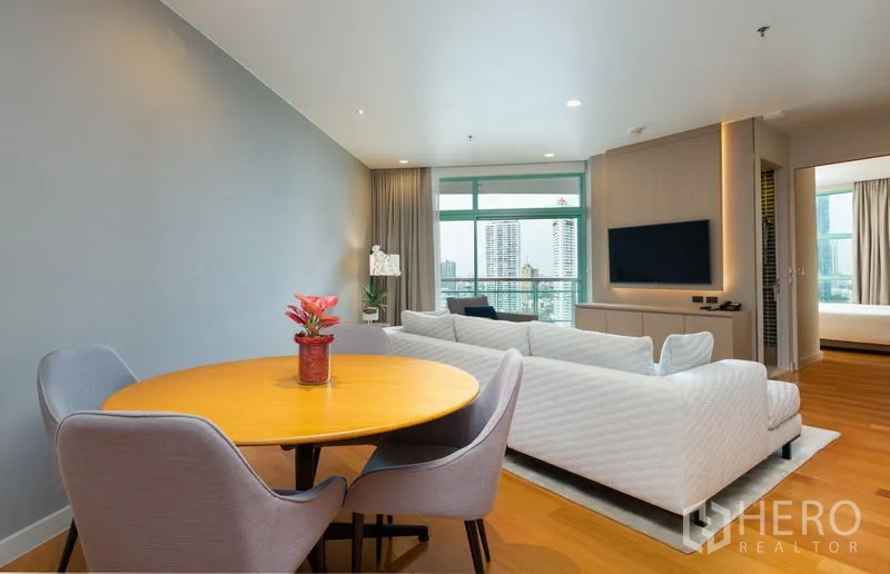 Condominium for rent in Bang Kho Laem, Bangkok - Open-plan living and dining area with round table, sofa set, TV wall and floor-to-ceiling windows overlooking the river skyline.