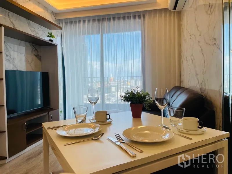 Condominium for rent in Bang Na, Bangkok - Dining table set by the TV console with sheer curtains leading to the balcony.