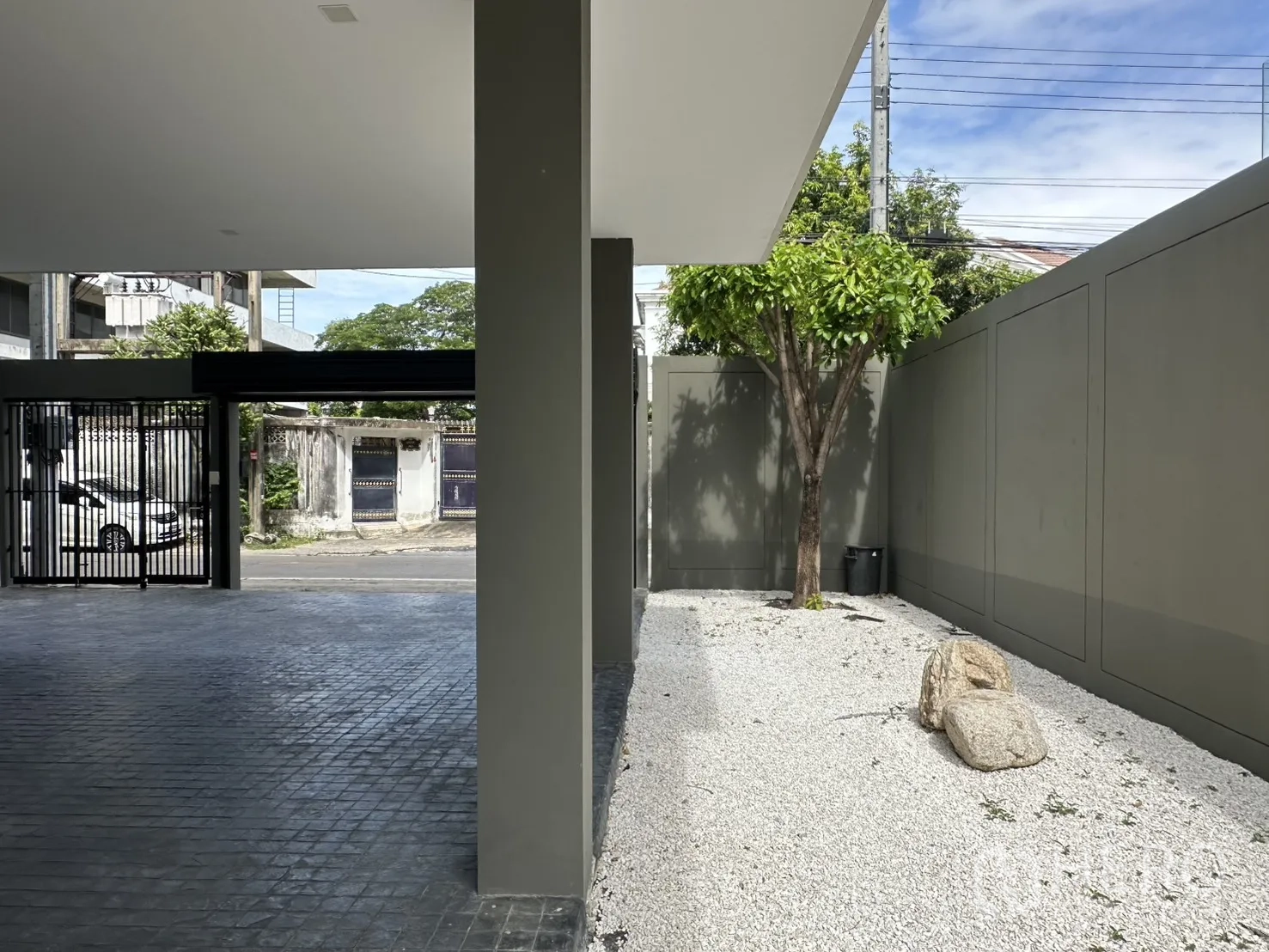 家庭办公室 for rent or sale in Suan Luang, Bangkok - 带顶棚的车道与黑色大门，旁有碎石庭院、树木与景观石。