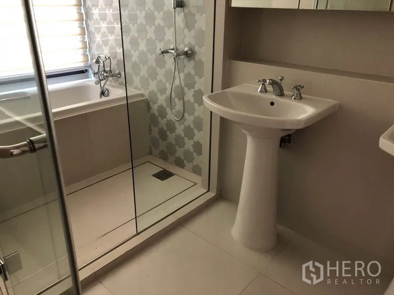 Condominium for rent or sale in Khlong Toei, Bangkok - Modern bathroom featuring a glass-enclosed shower, bathtub, and pedestal sink.