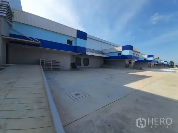 โรงงาน ให้เช่าในBang Lamung, Chon Buri - ท่าโหลดภายนอกพร้อมทางลาด ผนังโทนฟ้า–ขาว และลานคอนกรีตกว้าง