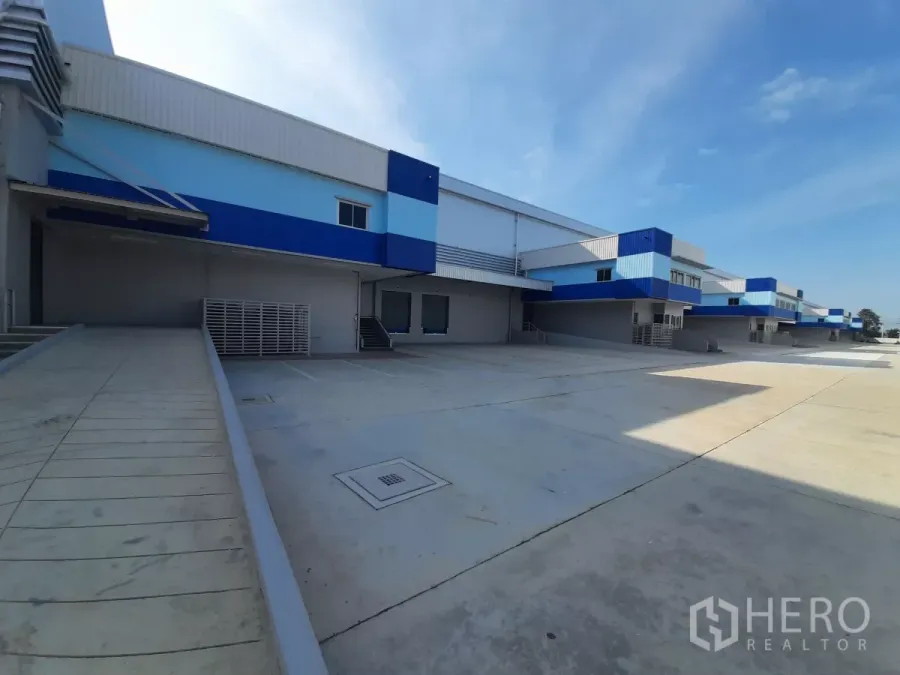 โรงงาน ให้เช่าในBang Lamung, Chon Buri - ท่าโหลดภายนอกพร้อมทางลาด ผนังโทนฟ้า–ขาว และลานคอนกรีตกว้าง