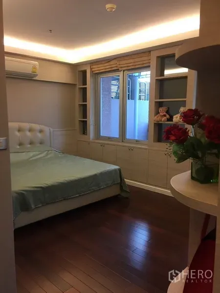 Condominium for rent in Bang Rak, Bangkok - Cozy bedroom with built-in shelving, window and warm wood flooring.