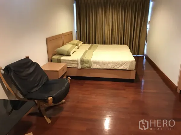 Condominium for rent in Khlong Toei, Bangkok - Spacious bedroom with double bed, black lounge chair and full-length curtains.