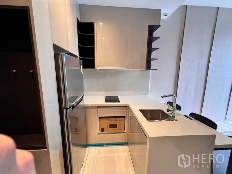 Condominium for rent in Watthana, Bangkok - Compact L-shaped kitchen with induction cooktop, upper cabinets and sink.