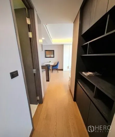 Condominium for rent in Khlong Toei, Bangkok - Hallway with wood flooring and built‑in dark shelving leading to dining area.