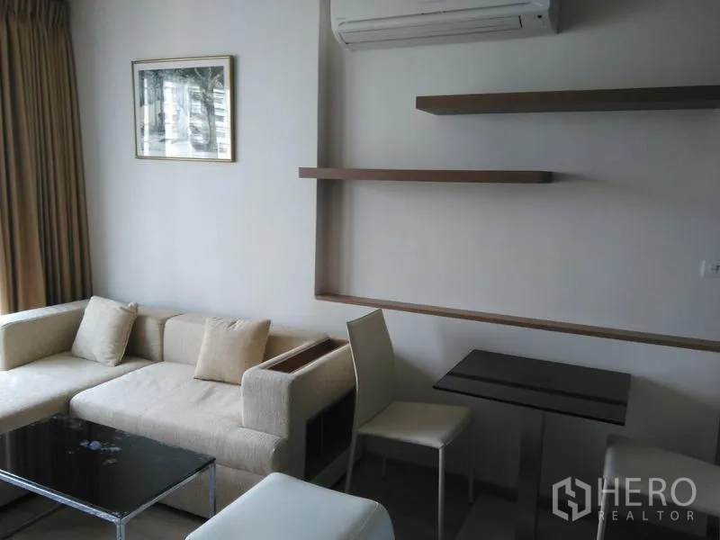 Condominium for rent in Sathon, Bangkok - Bright living area with cream sofa, floating shelves and compact dining set.