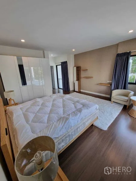 Detached House for rent or sale in Prawet, Bangkok - Sunlit bedroom with wardrobe, armchair and wood floors.