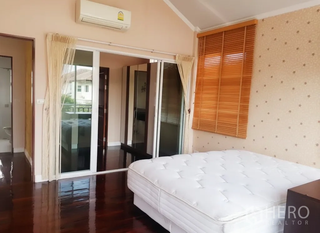Detached House for rent in Lat Krabang, Bangkok - Upstairs bedroom with sliding doors to a small balcony and wall-mounted air conditioner.