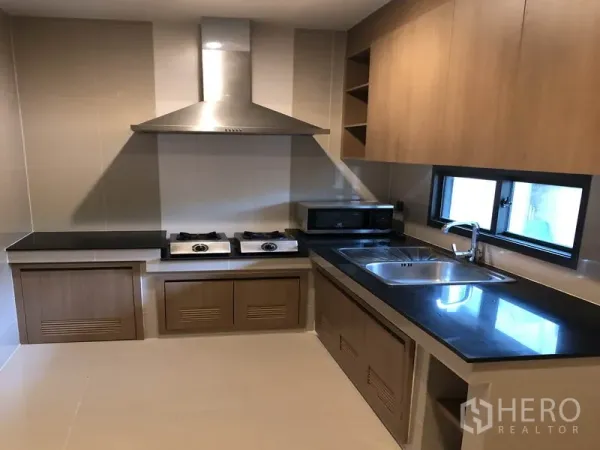 Detached House for rent in Bang Kapi, Bangkok - Built-in kitchen with black countertops, gas hobs, range hood and stainless sink.