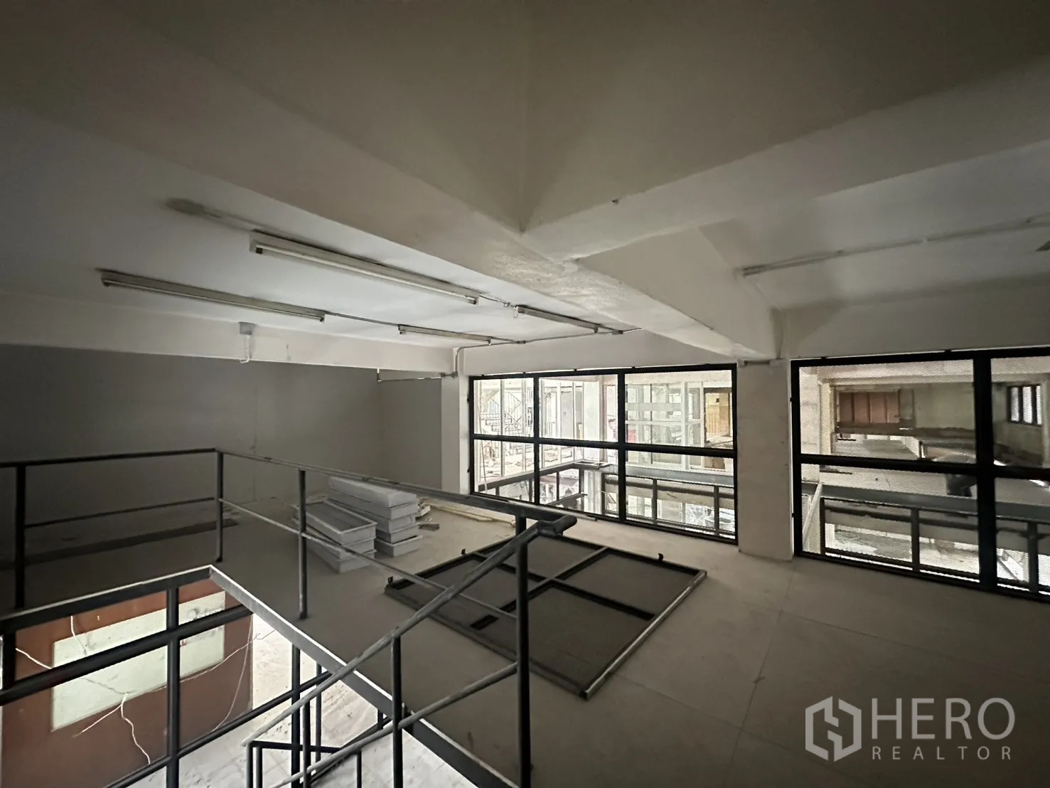 พื้นที่ขายของ for rent in Watthana, Bangkok - มุมชั้นลอยพร้อมราวเหล็ก ไฟฟลูออเรสเซนต์ และผนังกระจกบานใหญ่ที่มองออกไปยังอาคารโดยรอบ