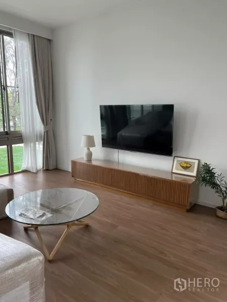 Detached House for rent in Saphan Sung, Bangkok - Bright living room with floor-to-ceiling windows, wood floors, TV wall and a glass coffee table.