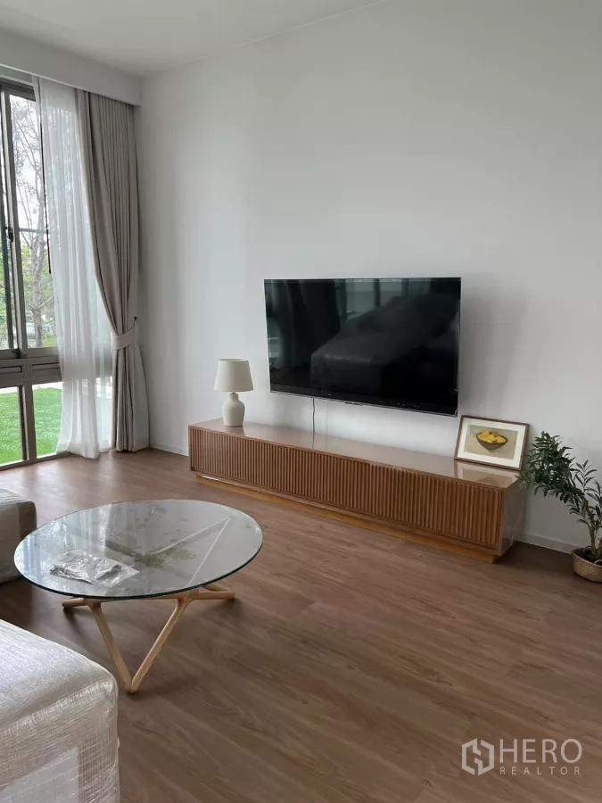 Detached House for rent in Saphan Sung, Bangkok - Bright living room with floor-to-ceiling windows, wood floors, TV wall and a glass coffee table.