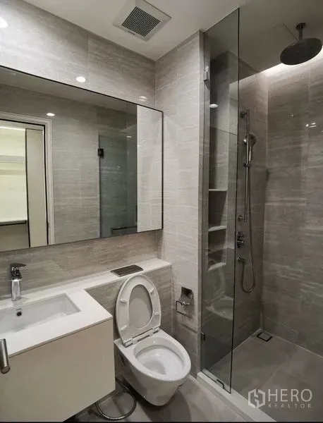Condominium for rent in Bang Rak, Bangkok - Modern bathroom with large mirror, vanity and a glass-enclosed rain shower.